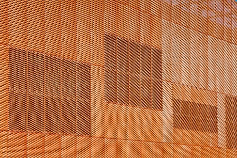 Die großen Fenster der Hallen zeichnen sich hinter der Fassadenhaut ab. Die Fassade besteht ausschließlich aus Streckmetall-Blechen.<br />