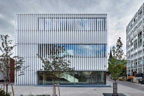 <span class="White">Zwei eingeschossige Sporthallen wurde auf dem engen Grundstück durch eine neue, dreigeschossige Halle am City-Ring ersetzt. Die vertikale Lamellenfassade wird durch die dahinterliegenden, horizontalen Fensterbänder gebrochen</span><br /><br />
