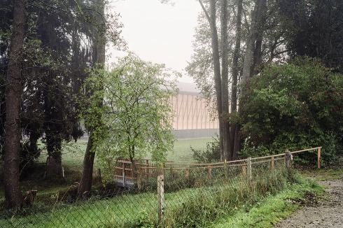 Die Sporthalle liegt mitten in Haiming und doch in der Landschaft. Zur Baumreihe am Bachlauf im Norden löst sich der Baukörper in ein filigranes Streben-Geäst auf.<br />