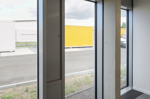 Die außen vorgetäuschte Dreigeschossigkeit führt zu unterschiedlichen Fassa­denausprägungen in den Büros des Erd- bzw. des Obergeschosses. Links die Eingangshalle, in der zum Zeitpunkt der Aufnahme noch fleißig gewerkelt wurde.<br />