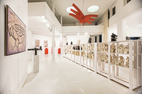 Die Skulpturen von Rob Krier sind in einem Regal mitten im Raum untergebracht. Ergänzt werden sie nicht nur durch die gewebten Bilder von Roswitha Grützke, sondern auch von den ab­strakten, in rot gehaltenen Architekturmodellen von François Valentiny.<br />