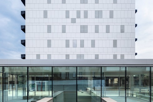 Die zwei Giebelseiten waren ohne Fenster. Nach langen Beratungen wurden Fenster zugelassen, wenn sie sich bündig in das bestehende Fugenraster einfügen. Allerdings wurde die Fassade komplett ausgetauscht. Durch die neue Dämmung nun etwas breiter geworden, mussten die Proportionen leicht verändert werden. Im Vordergrund der neue gläserne Eingangspavillon der Architekten<br />