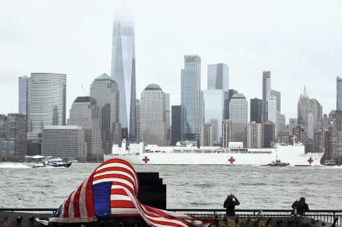 Symbolische Lage der Na­tion: eine gebeutelte US-Flagge vor der Skyline am Hudson River mit One World Trade Center und La­za­rettschiff USNS Comfort<br />