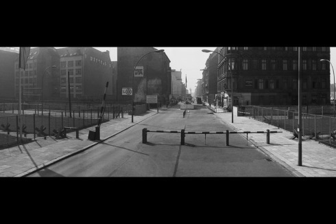 [Checkpoint Charlie, 15.12 Uhr] Ein US-Soldat hält von der Checkpointbaracke aus ein circa 25 x 30 cm großes Aktfoto hoch.<br />
