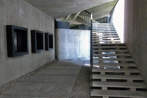 Der Eingangsbau besteht aus rau geschaltem Beton, im Treppenaufgang werden in Wandvitrinen Grafiken ehemaliger Häftlinge gezeigt.<br />