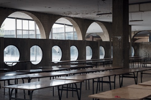 Große Halle der Mensa hinter einer internen Betonwand mit Rundfenstern. <br />