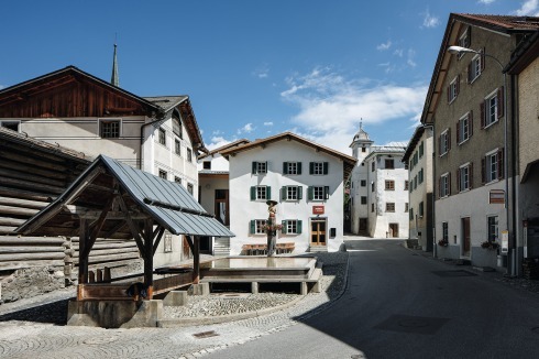Dorfplatz von Valendas mit dem, so heißt es, größten Holzbrunnen Europas. In der Mitte das „Gasthaus am Brunnen“. Von Caminadas Anbau links daneben ist eigentlich nur die Treppe hinauf in den Saal zu sehen.<br />